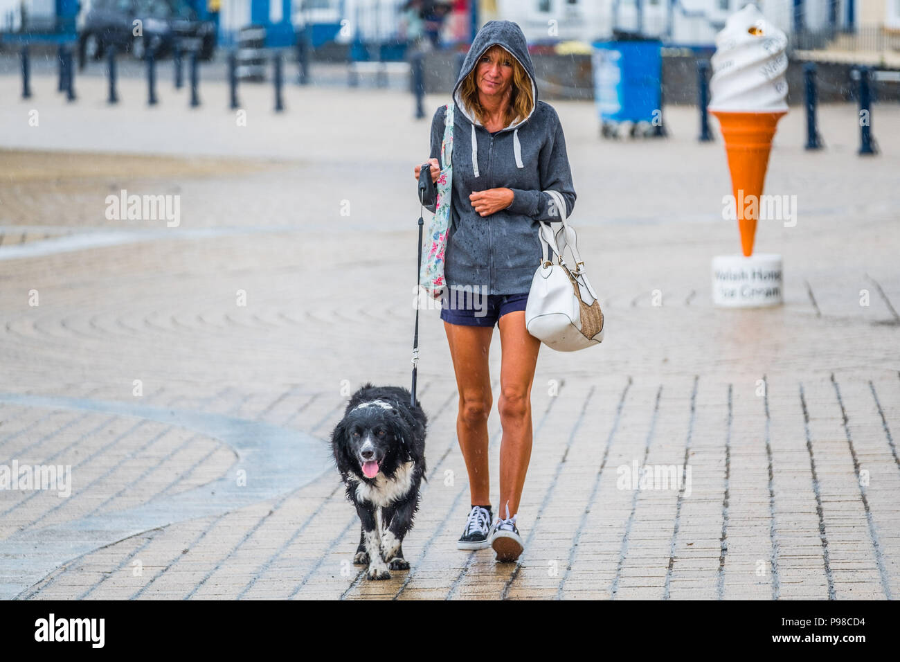 Aberystwyth Wales UK, Monday 16 July 2018  UK Weather: After many weeks of almost constant sunshine and exceptionally dry weather, the rains have returned with a woman seen  getting soaked as she walks with her dog  along the promenade in Aberystwyth on the west Wales coast  Photo credit: Keith Morris  Alamy Live News Stock Photo