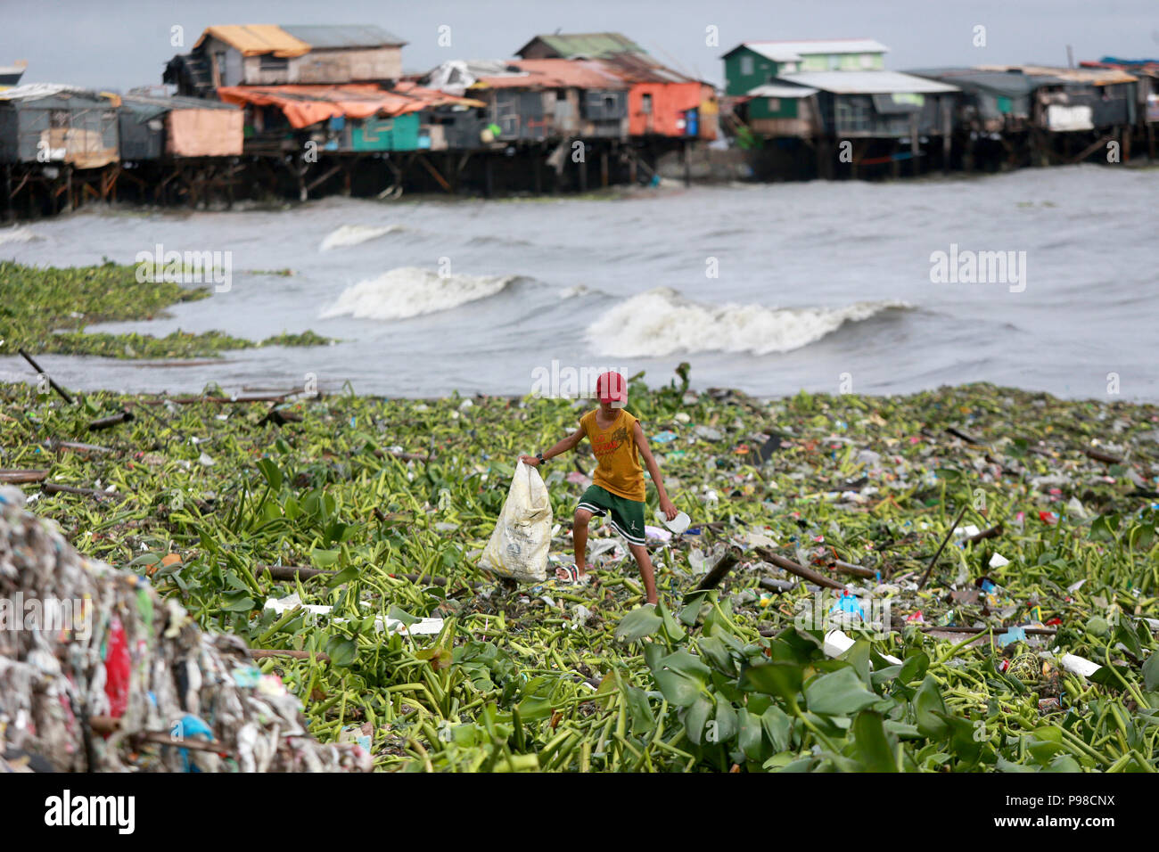 Manila, Philippines. 16th July, 2018. A child walks on water lilies and garbage as he gathers reusable materials washed ashore by the tropical depression Henry in Manila, the Philippines, July 16, 2018. Credit: Rouelle Umali/Xinhua/Alamy Live News Stock Photo