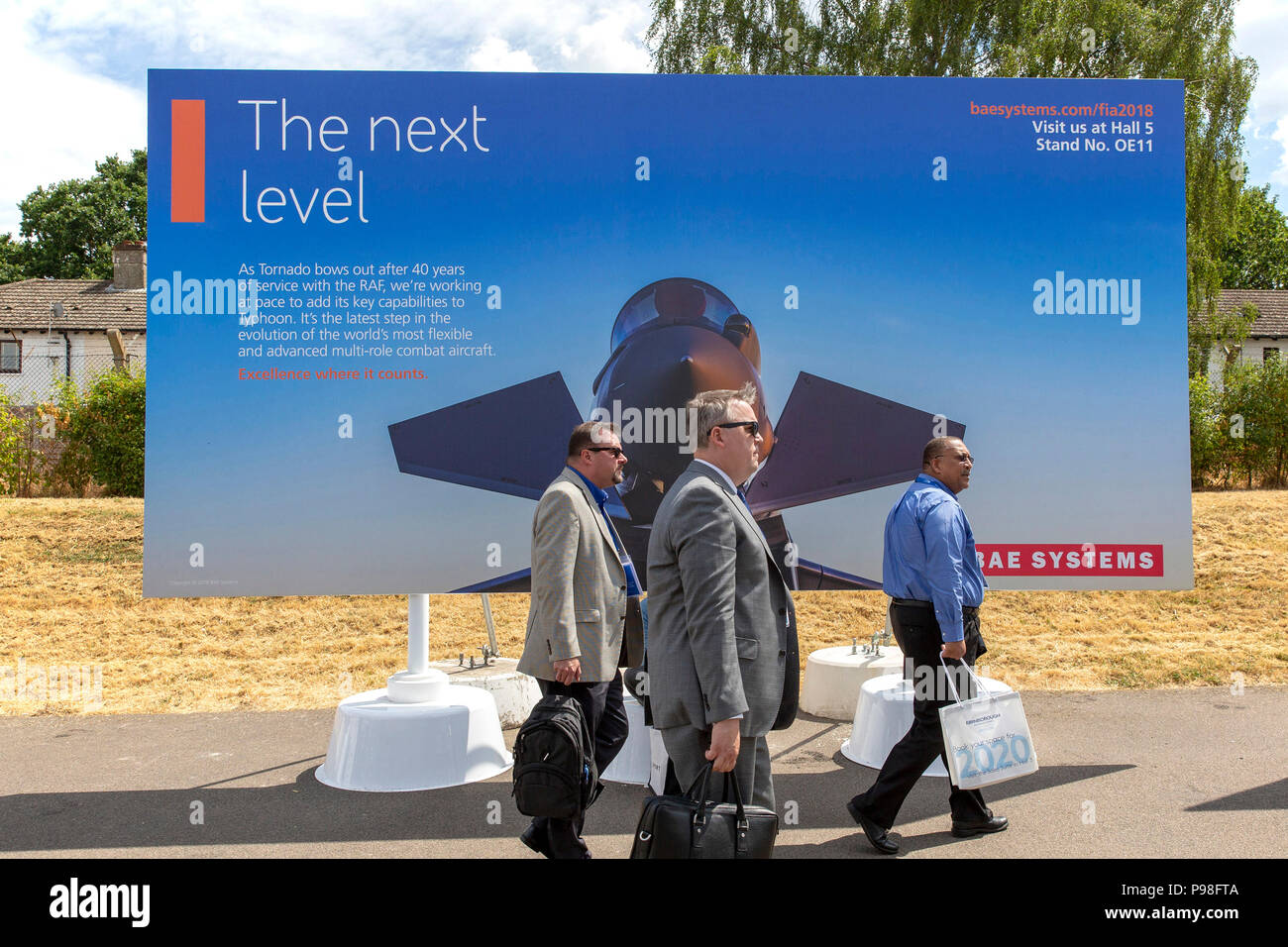 Farnborough Airshow 2018 17th July Three Men Walk Past A BAE Systems Advertisement Hoarding At Trade Day