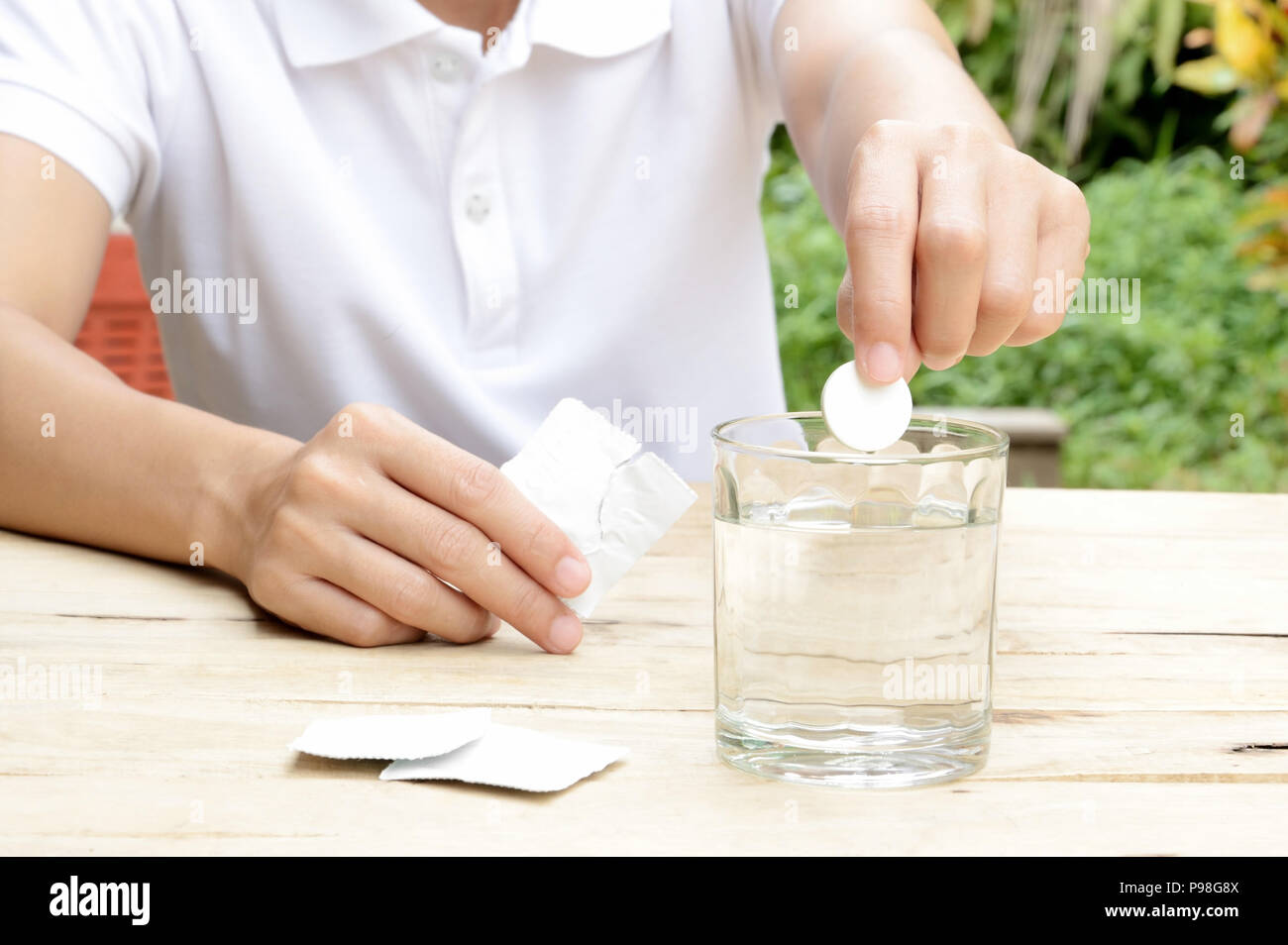 woman dropping effervescent tablet in glass of water on wooden table Stock Photo