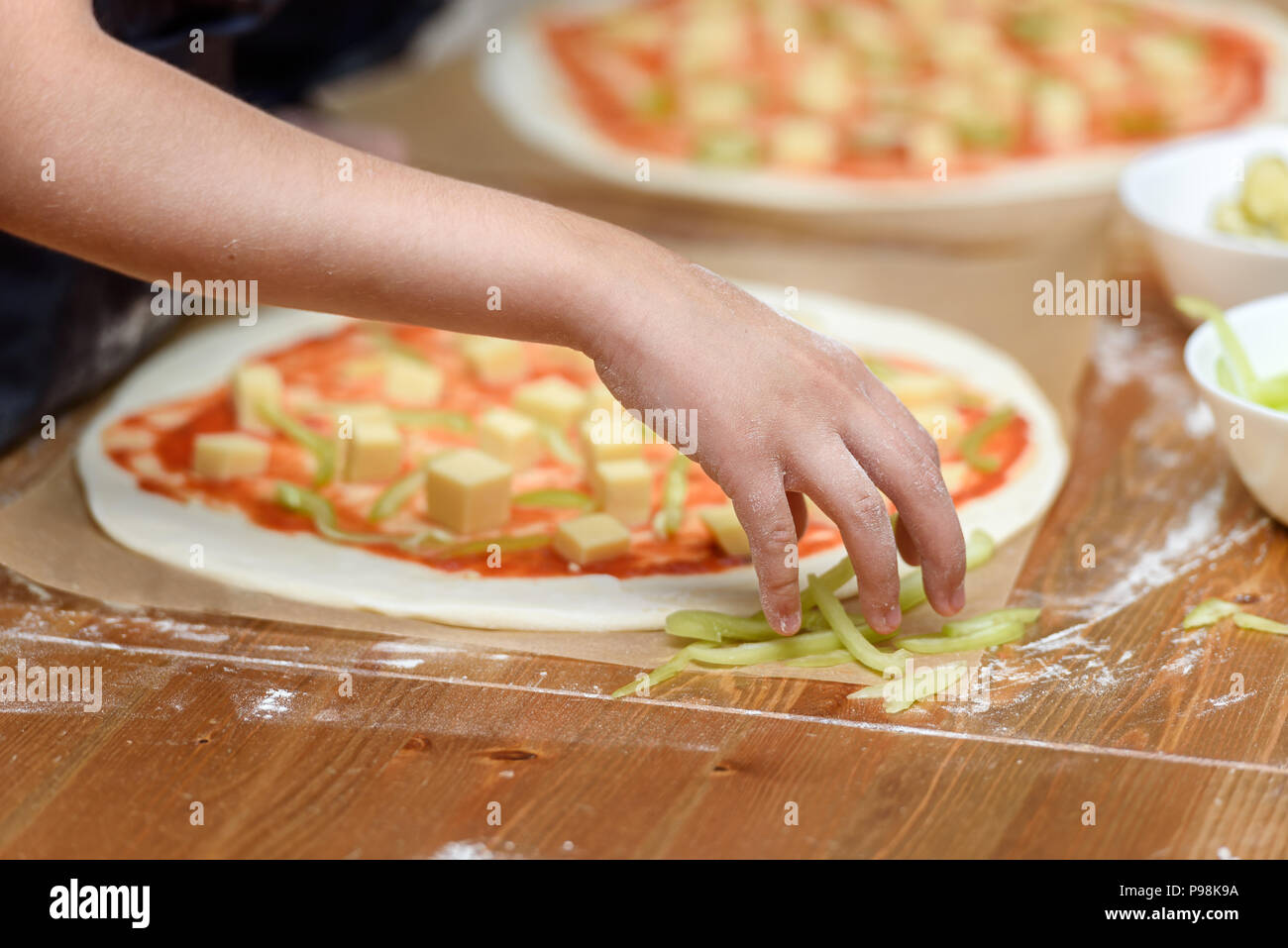 Close-up of children's hands preparing pizza. Children lay out on the basis of pizza vegetables and cheese Stock Photo