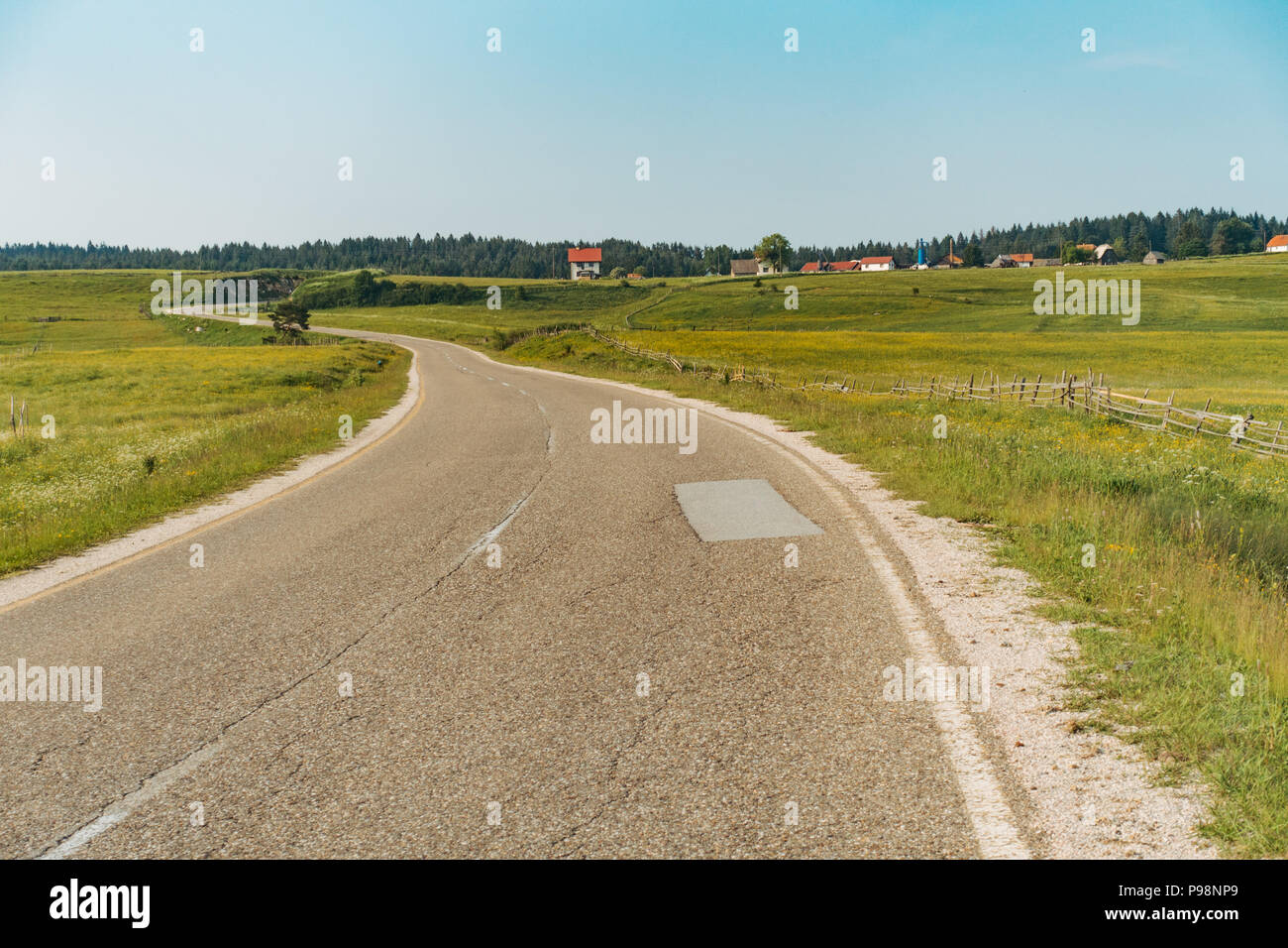 A countryside road passes by lush green fields of Bosnia and Herzegovina in summertime Stock Photo