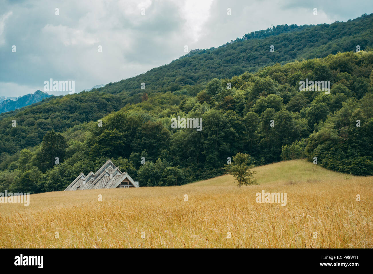 The unusual postmodern triangular lines of the Spomen-Dom (Memory House) designed by Ranko Radović peek over a field in Sutjeska National Park, BiH Stock Photo
