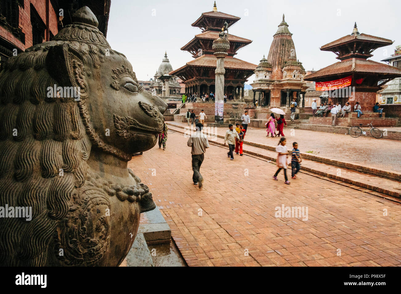 Lalitpur, Kathmandu Valley, Nepal : Passersby walk along the Unesco listed Patan Durbar square. A Royal Palace´s lion statue is seen in foreground and Stock Photo