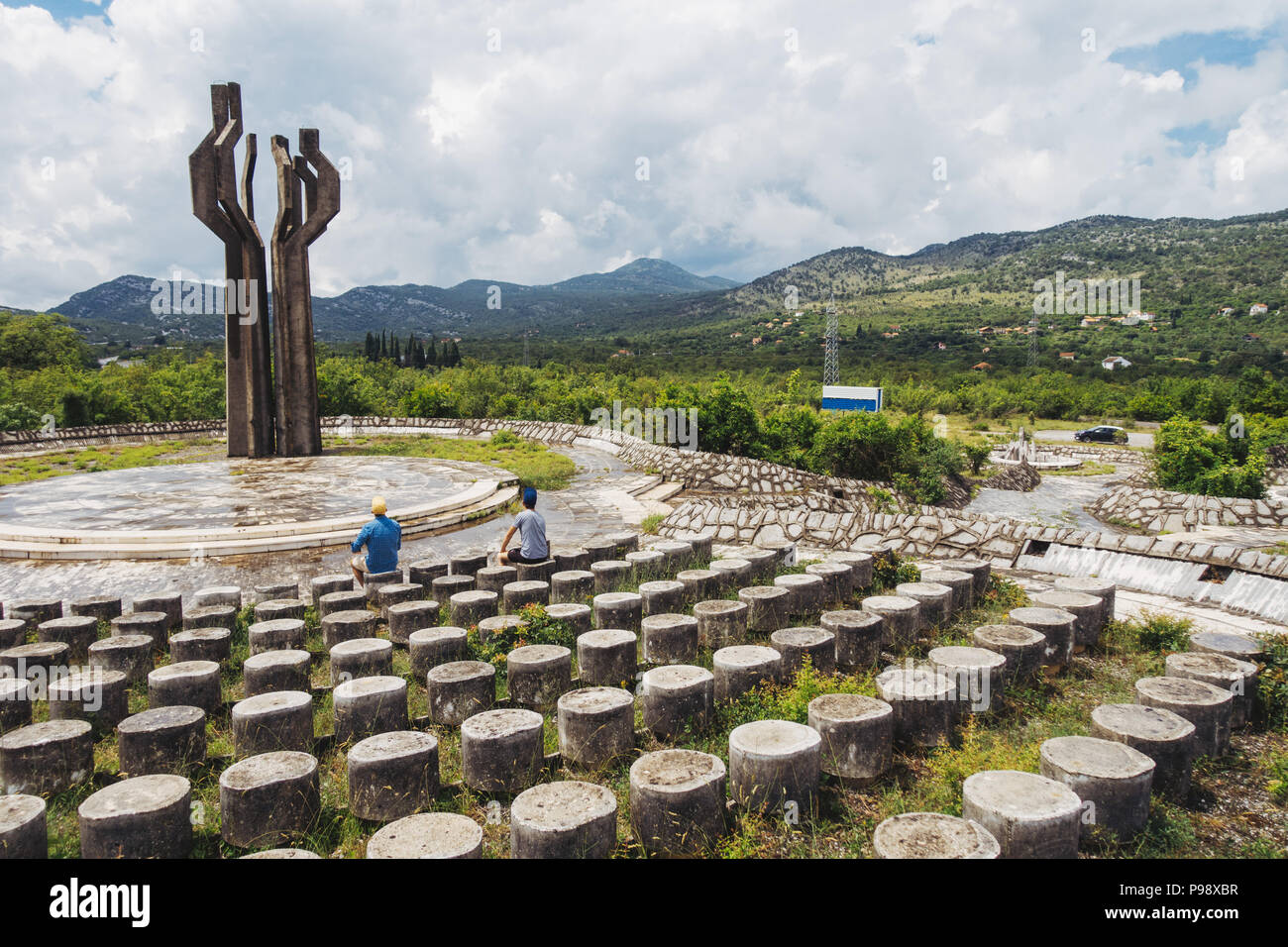 Tourists admire the 12 meter tall concrete Memorial to the Fallen of the Lješanska Nahija Region, near Kotor, Montenegro. Built in 1980 Stock Photo