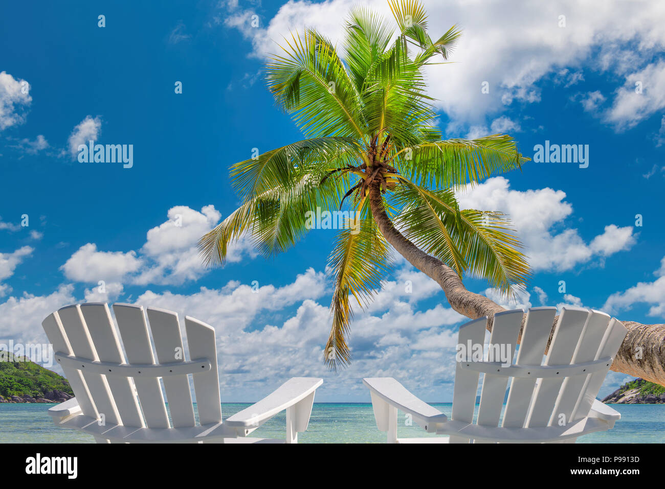 Beach chairs on sandy beach with palm and turquoise sea. Stock Photo
