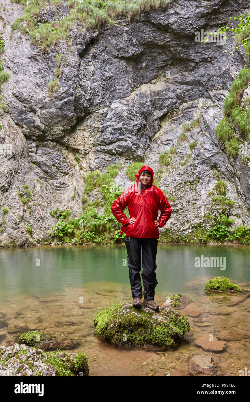Happy girl in raincoat by a karstic spring after hiking Stock Photo