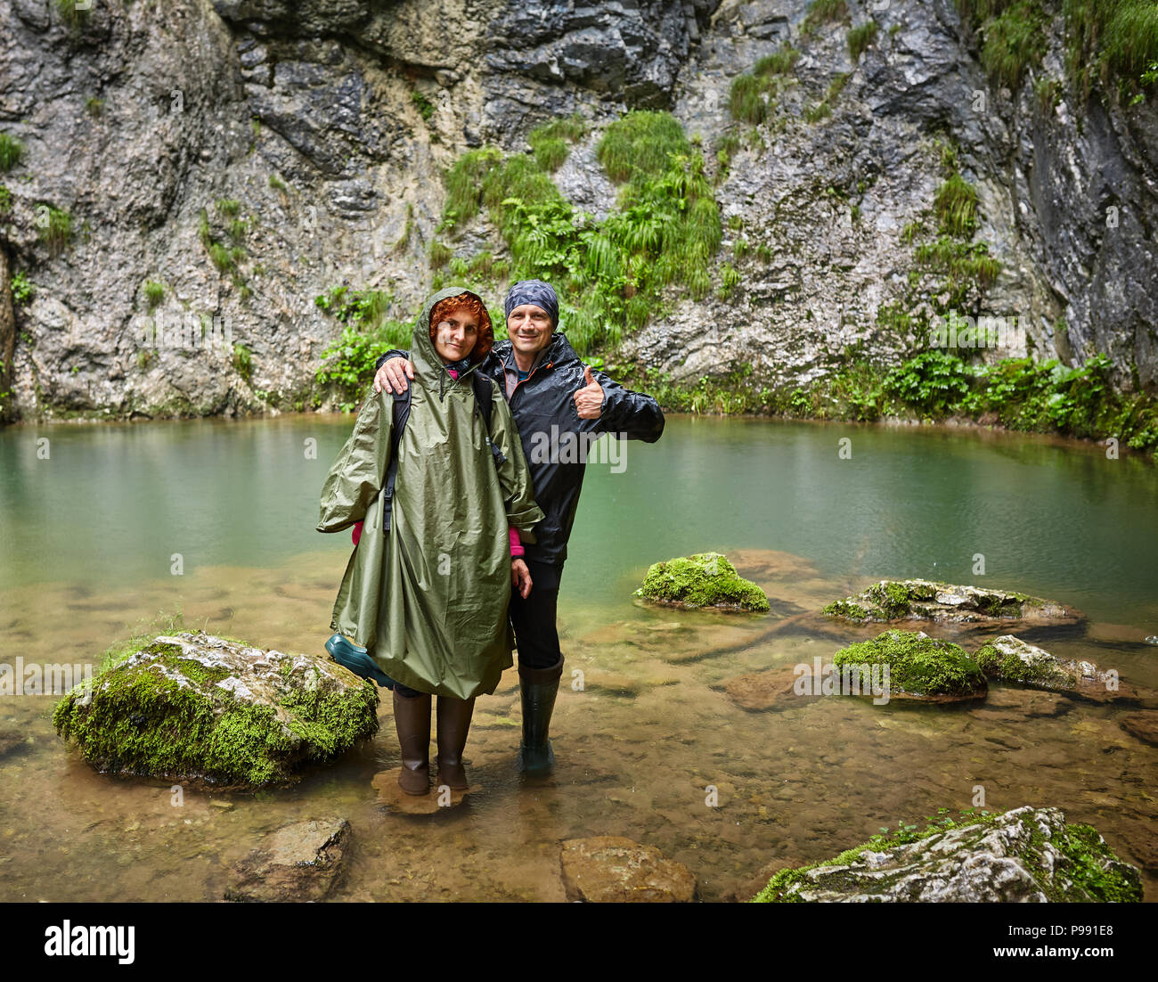 Couple in raincoats posing by a karstic spring Stock Photo