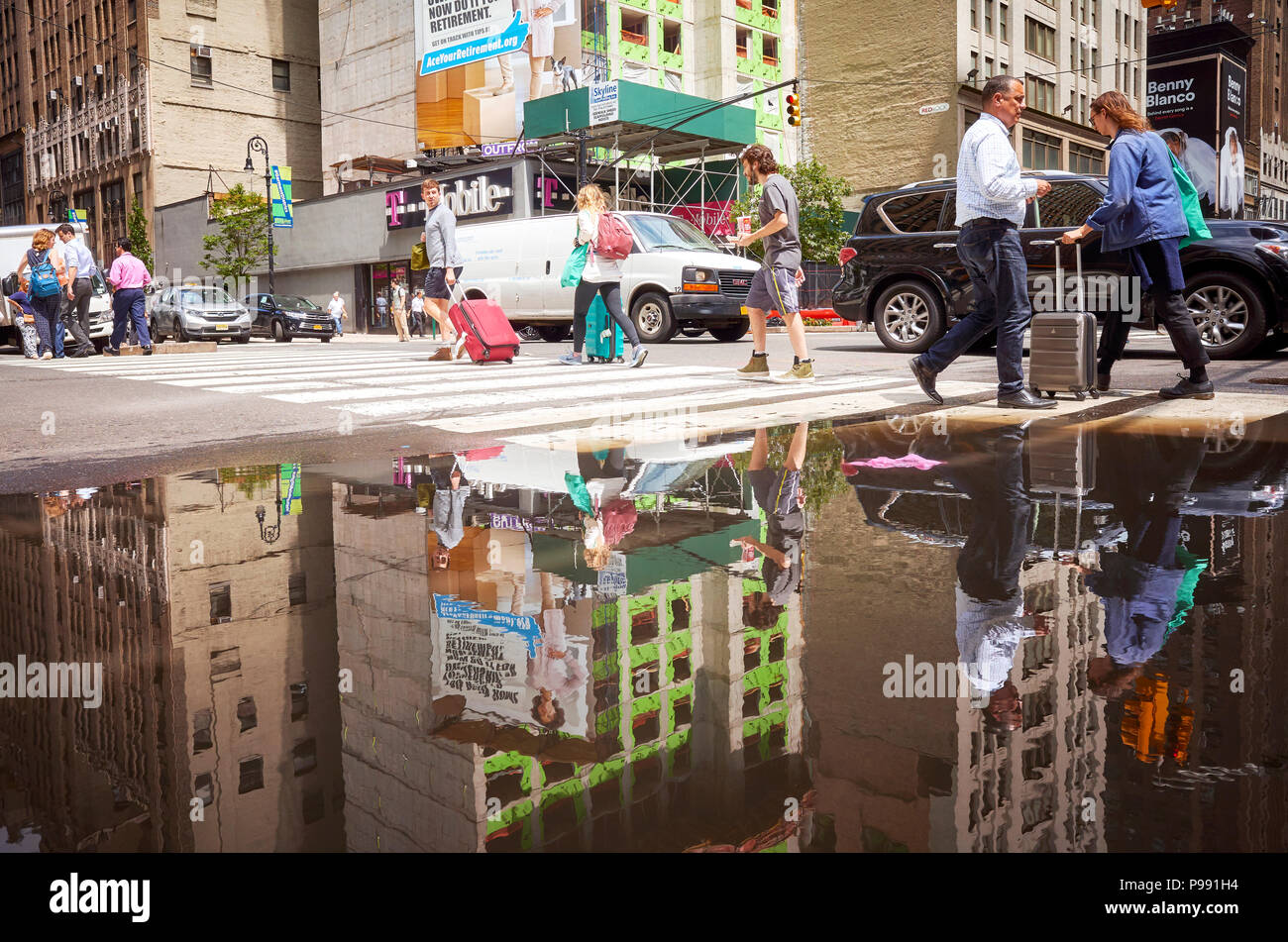New York City, USA - June 28, 2018: People walking through pedestrian crossing reflected in a puddle in Midtown Manhattan. Stock Photo