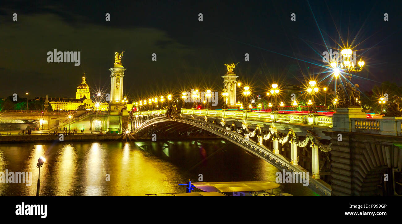 Panorama of Paris lights on in Pont Alexandre III bridge with lighted lamps. French European capital in Parisian night skyline of France. Night urban wide scene. Stock Photo