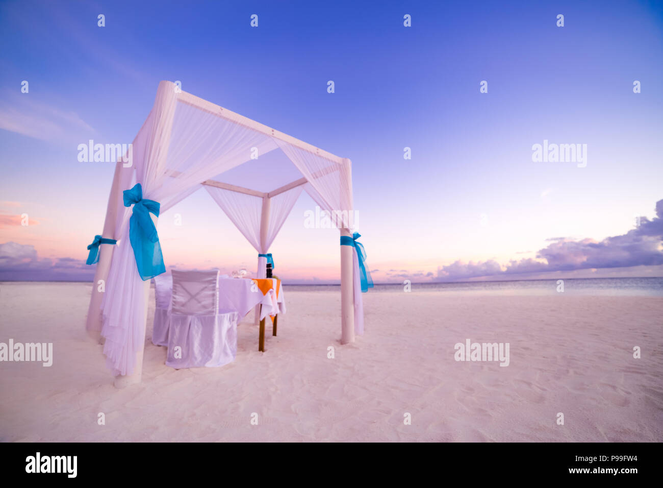 Romantic dinner table set-up for a honeymoon couple on the beach under sunset sky. Exotic wedding and honeymoon concept Stock Photo