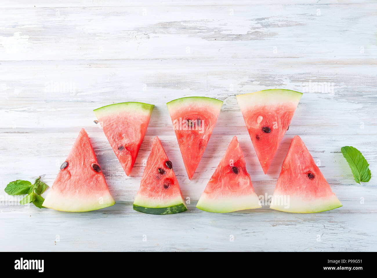 triangular Slices of watermelon lined up in a row on white wooden table ...