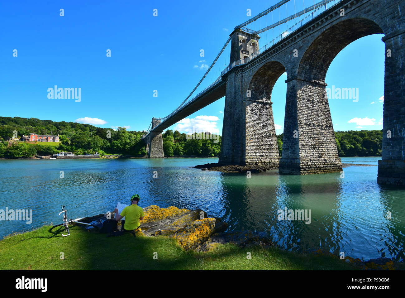 Cyclist reading a map below the Menai Bridge spanning the Menai Strait