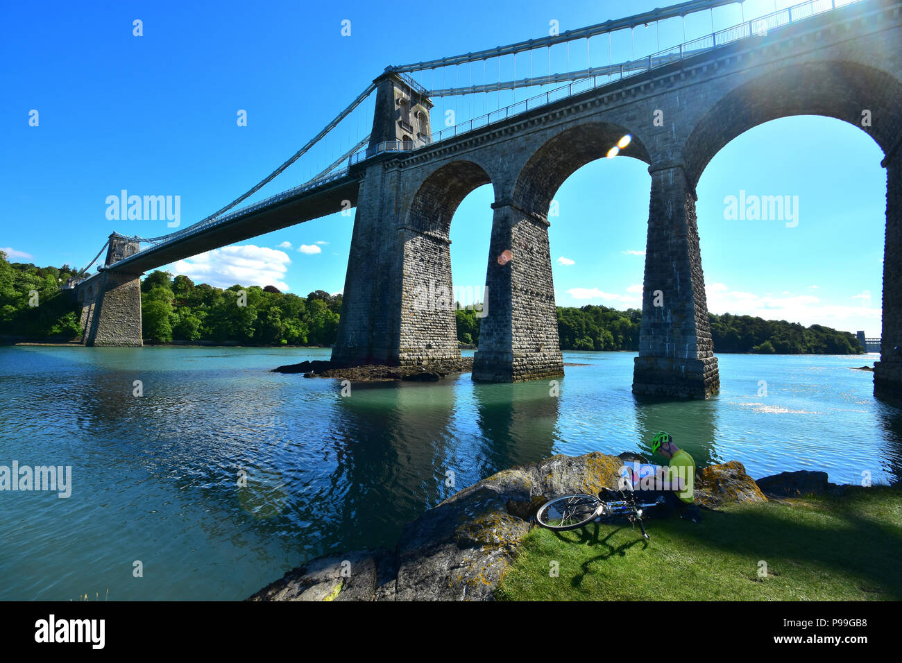 Cyclist reading a map below the Menai Bridge spanning the Menai Strait