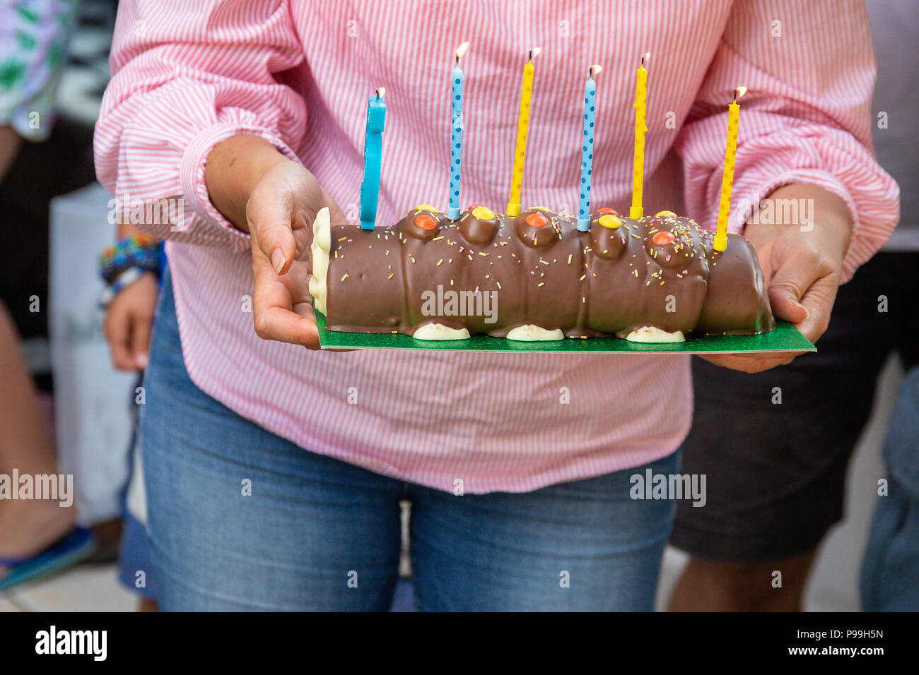 A woman carrying a chocolate log birthday cake with six lit candles Stock Photo