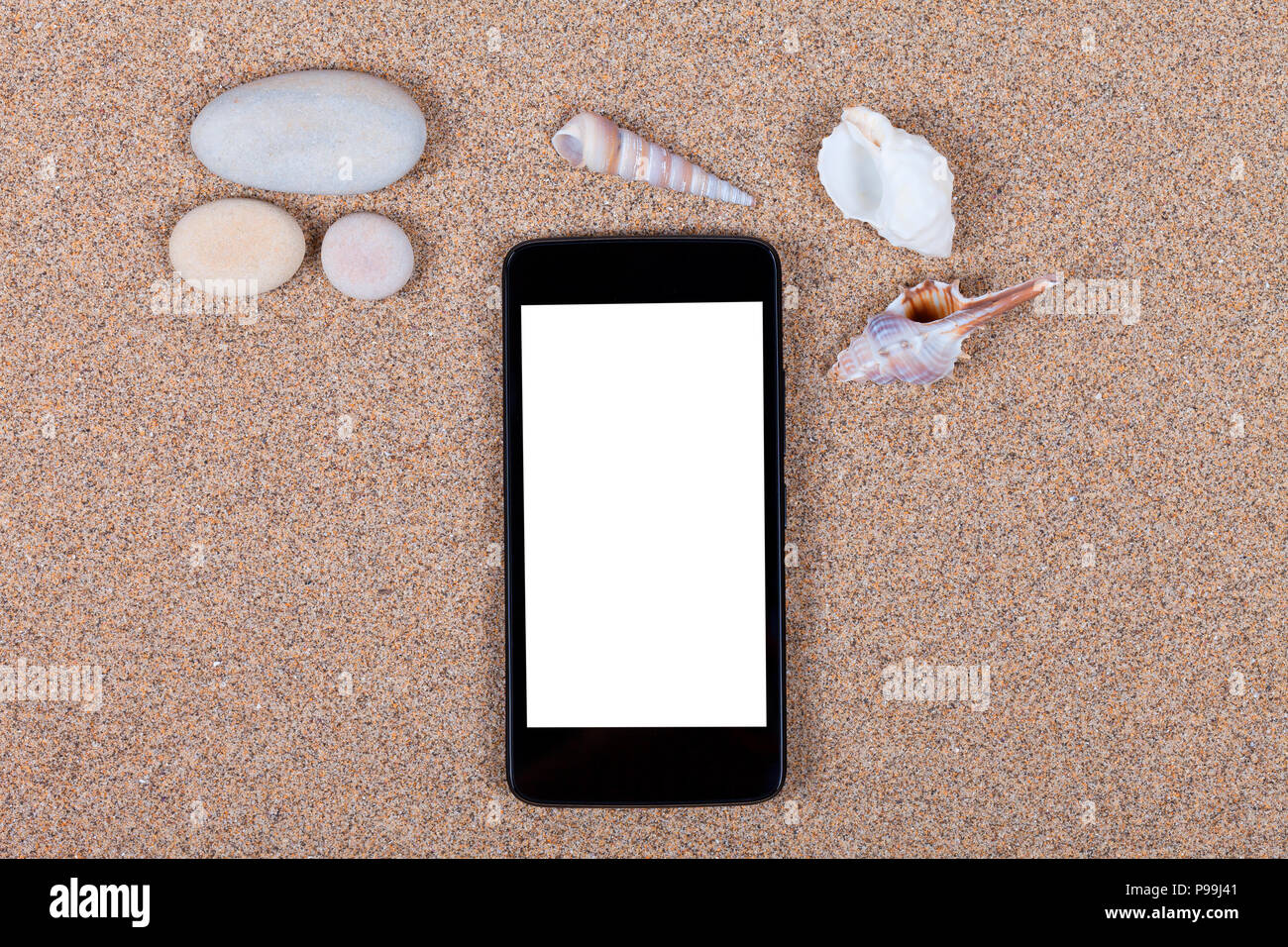 A smartphone with the blank screen placed on top of beach sand with shells and stones. Stock Photo