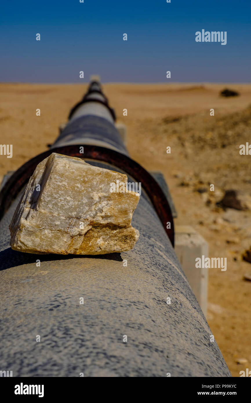 Focus on piece of silica rock on iron pipe stretching to horizon in Namib Desert carrying water supply from desalination plant in Swakopmund to uraniu Stock Photo