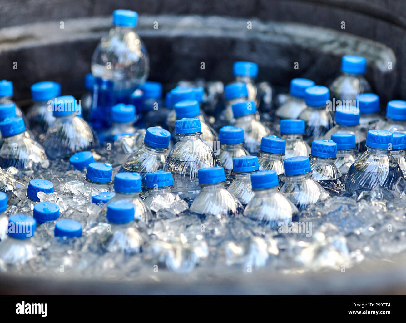 Plastic bottles of drinking water with blue caps floating in ice in a barrel Stock Photo