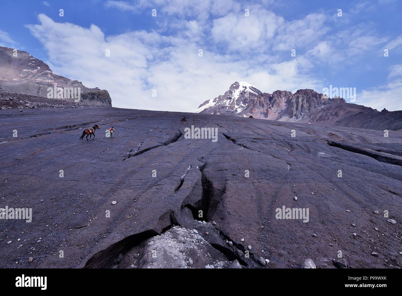 Carrier with the horse climbing on the Gergeti glacier, Stepantsminda, Georgia, Kazbek mountain Stock Photo