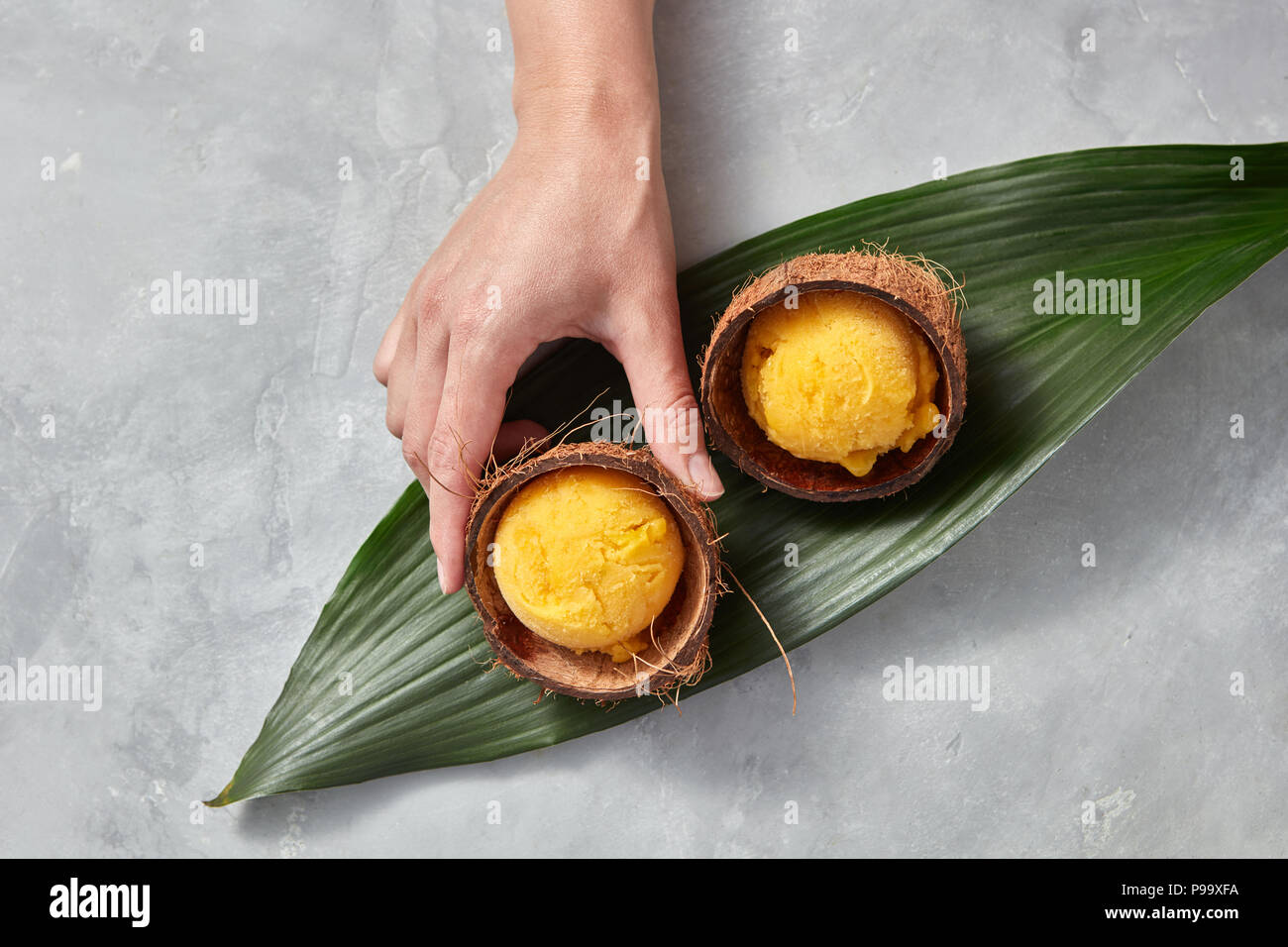 Homemade fruit ice cream in a coconut shell on a palm leaf on a gray ...