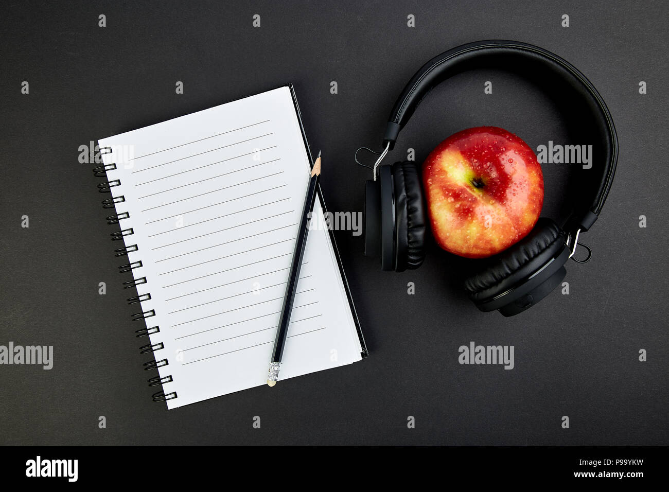 Black Headphones and red apple with notebook, note on black background ...