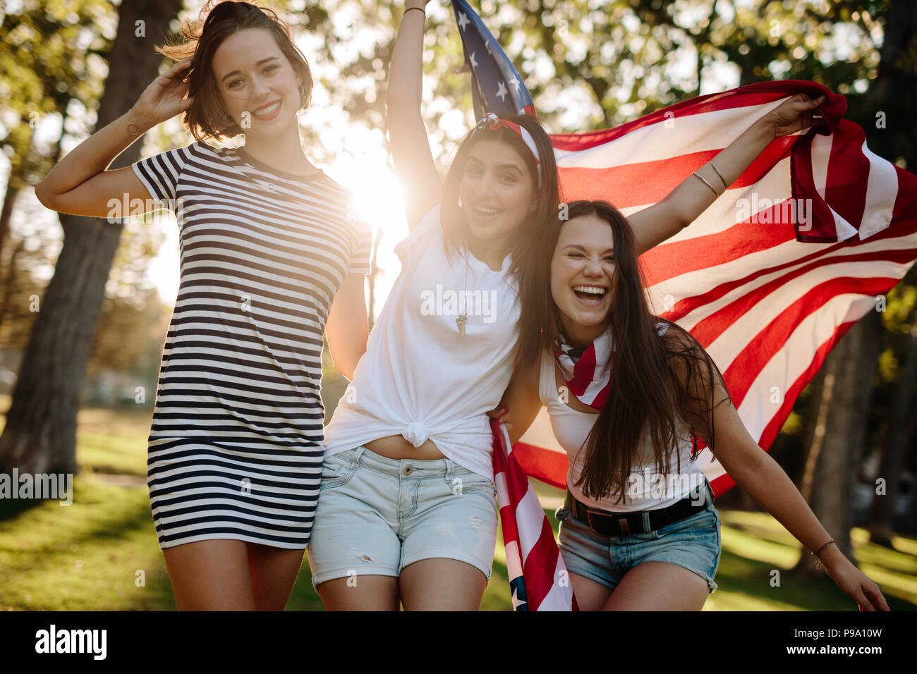 Portrait of three young women standing outdoors holding American flag ...