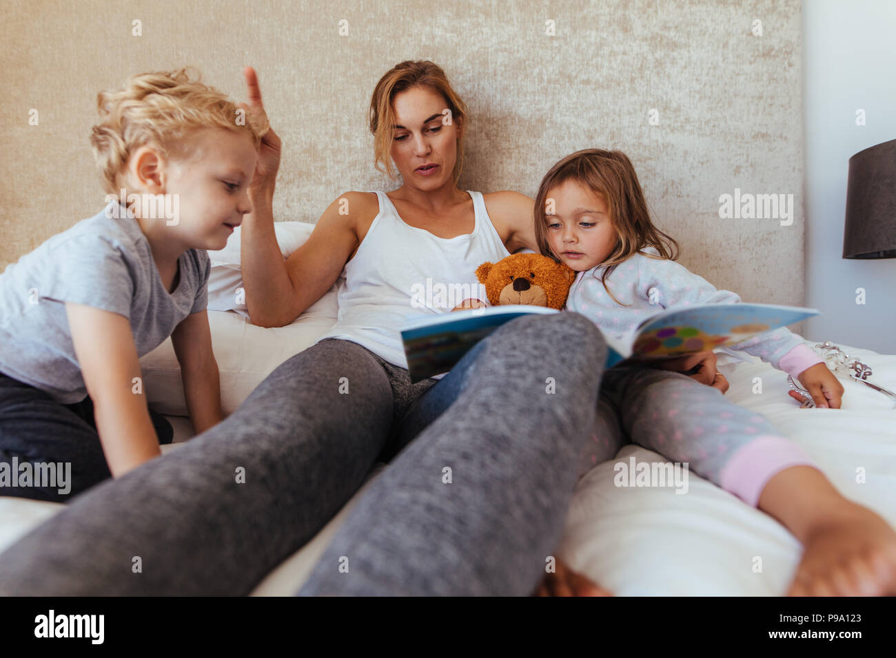 Mother reading bedtime story to children at home. Caring mother reading book for adorable little kids on bed. Stock Photo