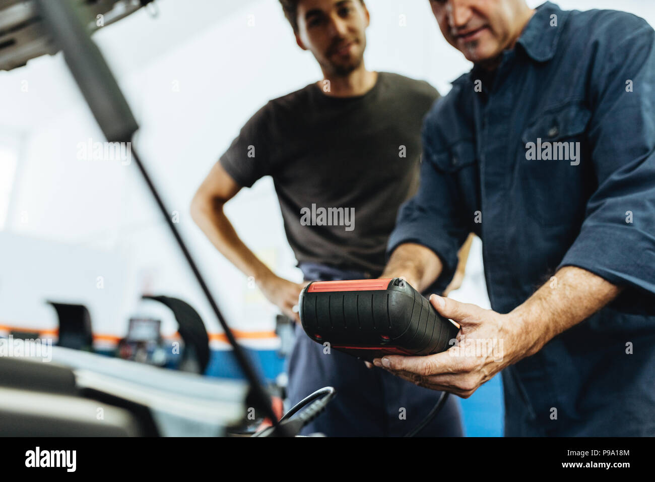 Automobile mechanics holding a device for checking engine condition. Mechanics diagnosing a car engine with device in service station. Stock Photo