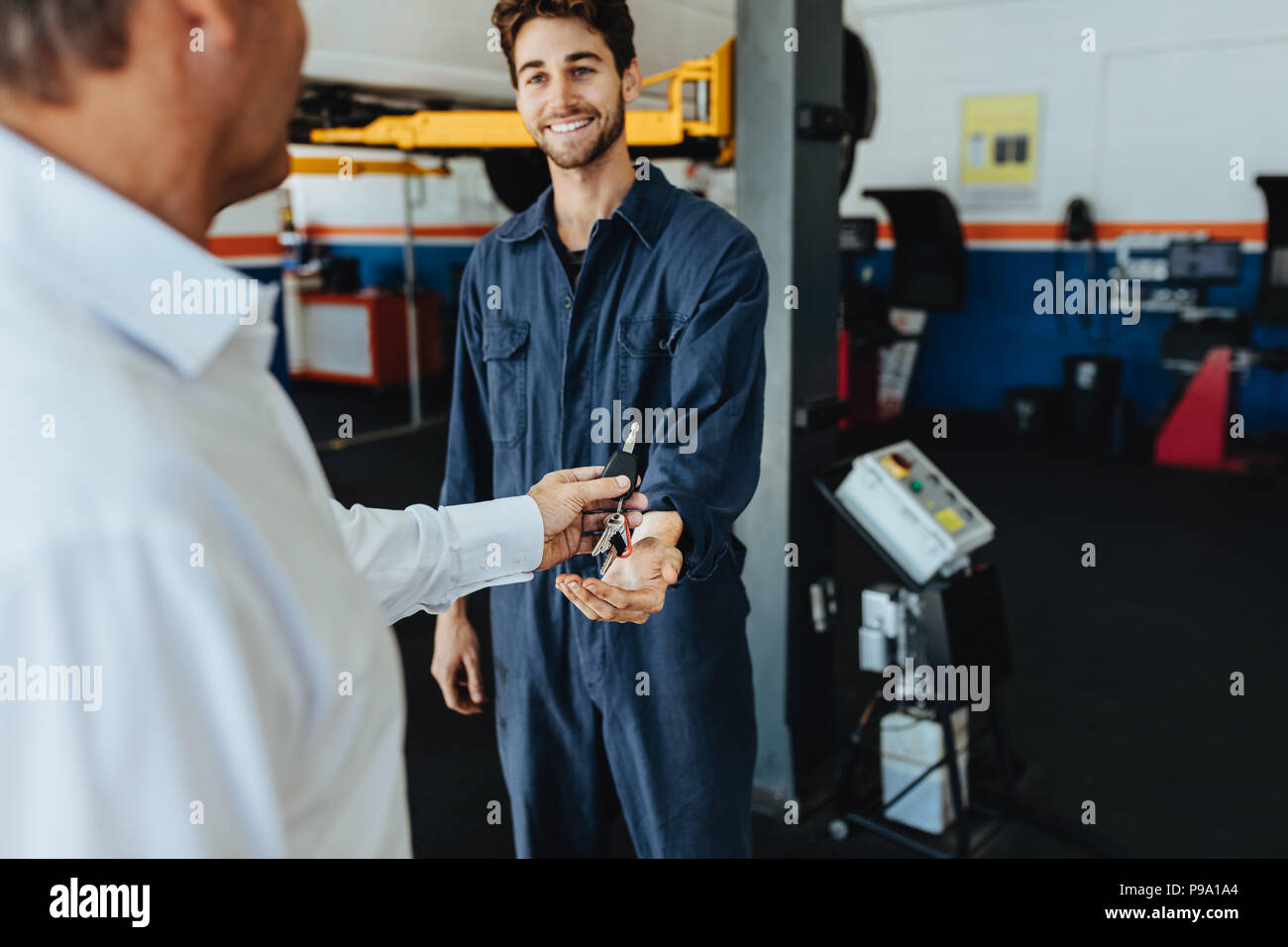 Mechanic receiving car keys from customer in automobile service center. Customer giving his car keys to mechanic at the repair garage. Stock Photo
