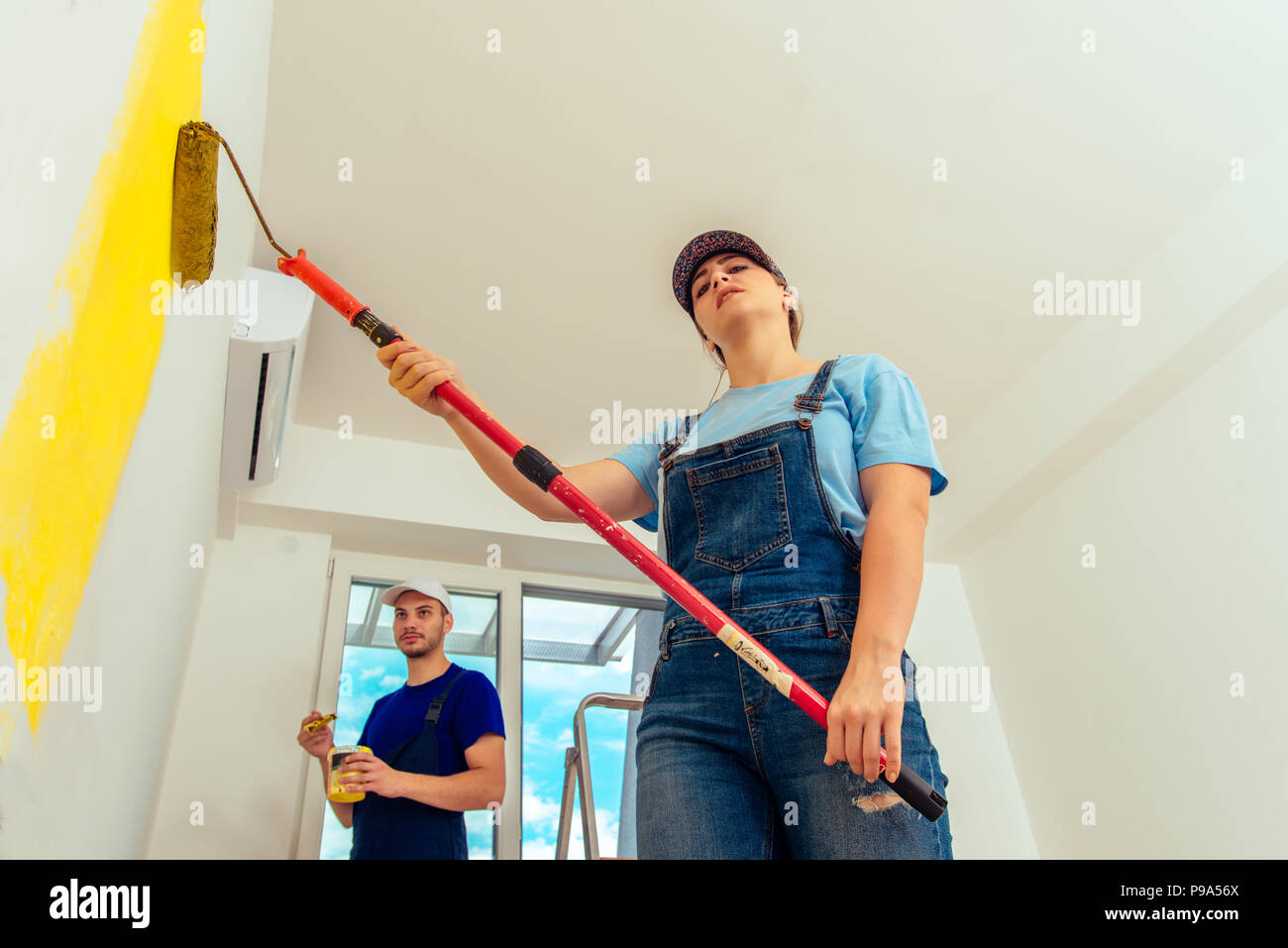 Couple decorating room using paint rollers and paintbrush on wall Stock Photo