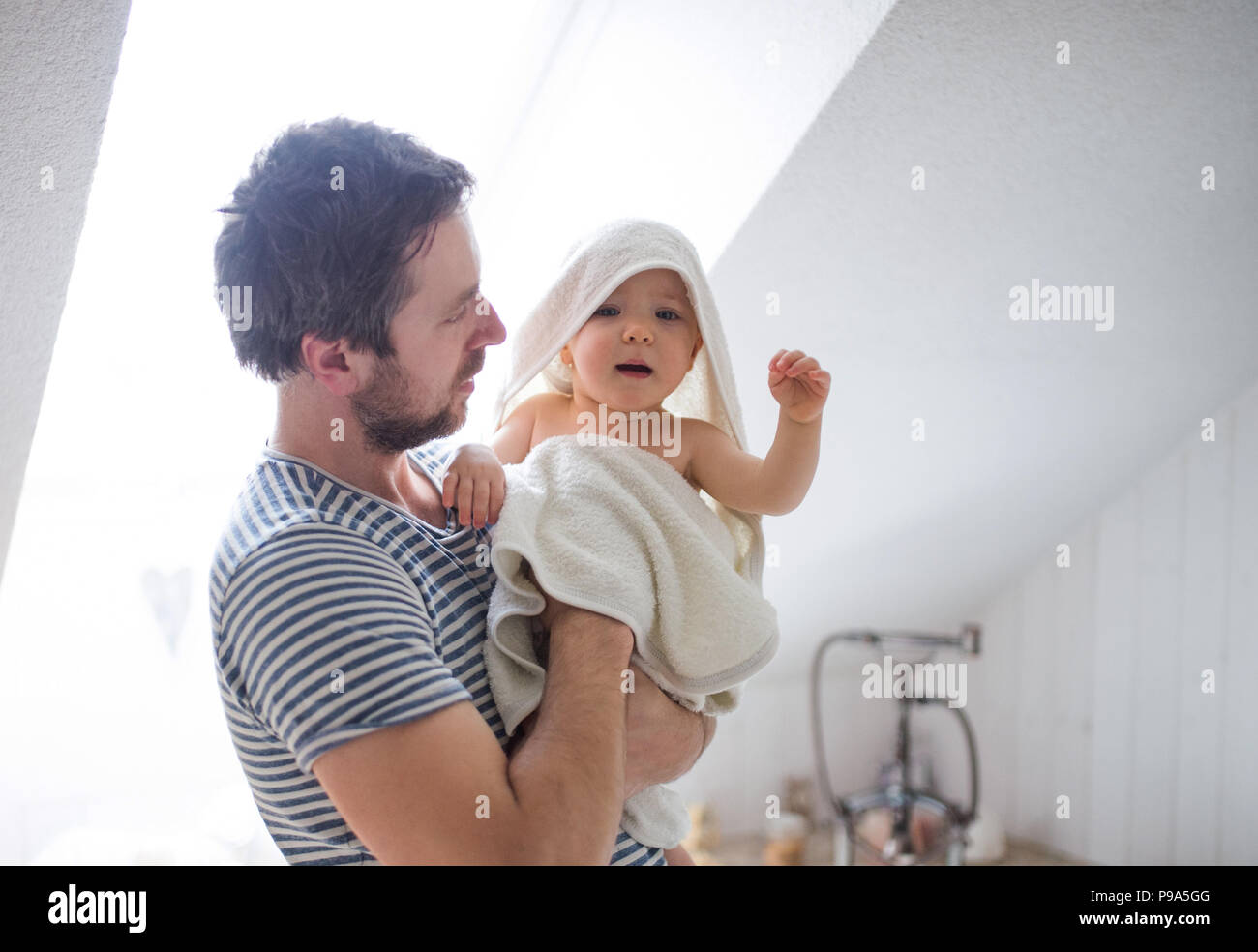 Father with a toddler child wrapped in towel in a bathroom at home. Stock Photo