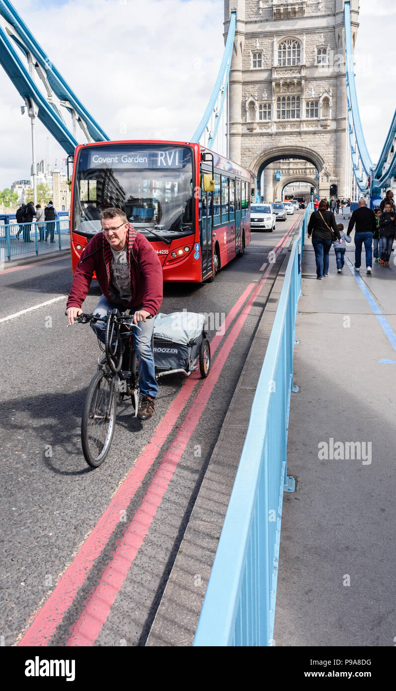 Head on portrait view of a cyclist about to be overtaken by a London red bus travelling across Tower Bridge Stock Photo