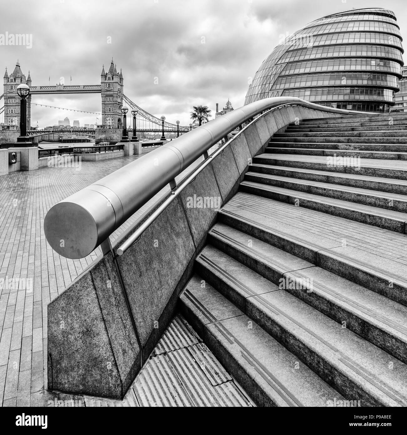 Close up black and white portrait view of steps and hand rail leading up to restaurants and City Hall at More London, with Tower Bridge on the left Stock Photo