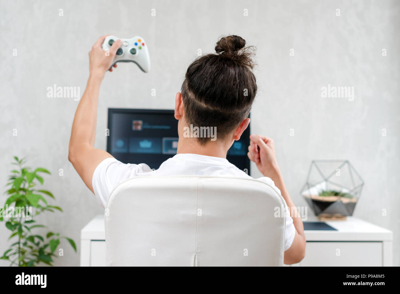 Happy young man playing and winning online game on computer. Back view of  gamer with video console gamepad controller. Competitive gaming, electronic  sports, technology, gaming, entertainment concept., Stock image