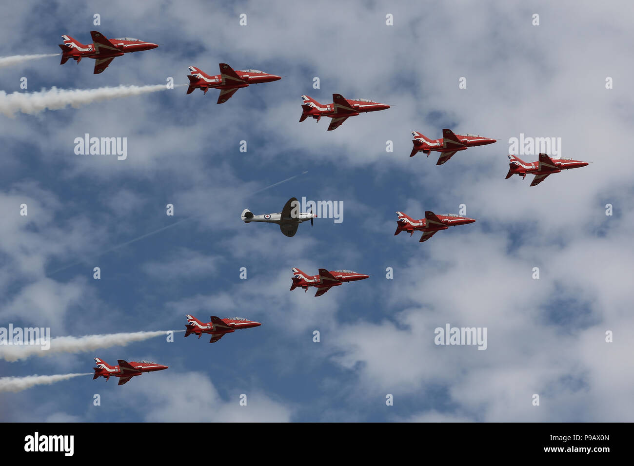 Farnborough, UK. 16th July 2018. The Royal Air Force Aerobatic Team, the Red Arrows, perform a flypast with a Supermarine Spitfire to open the 2018 Farnborough International Airshow, one of the biggest aviation trade and industry events in the world, held in the UK. Credit: James Hancock/Alamy Live News Stock Photo