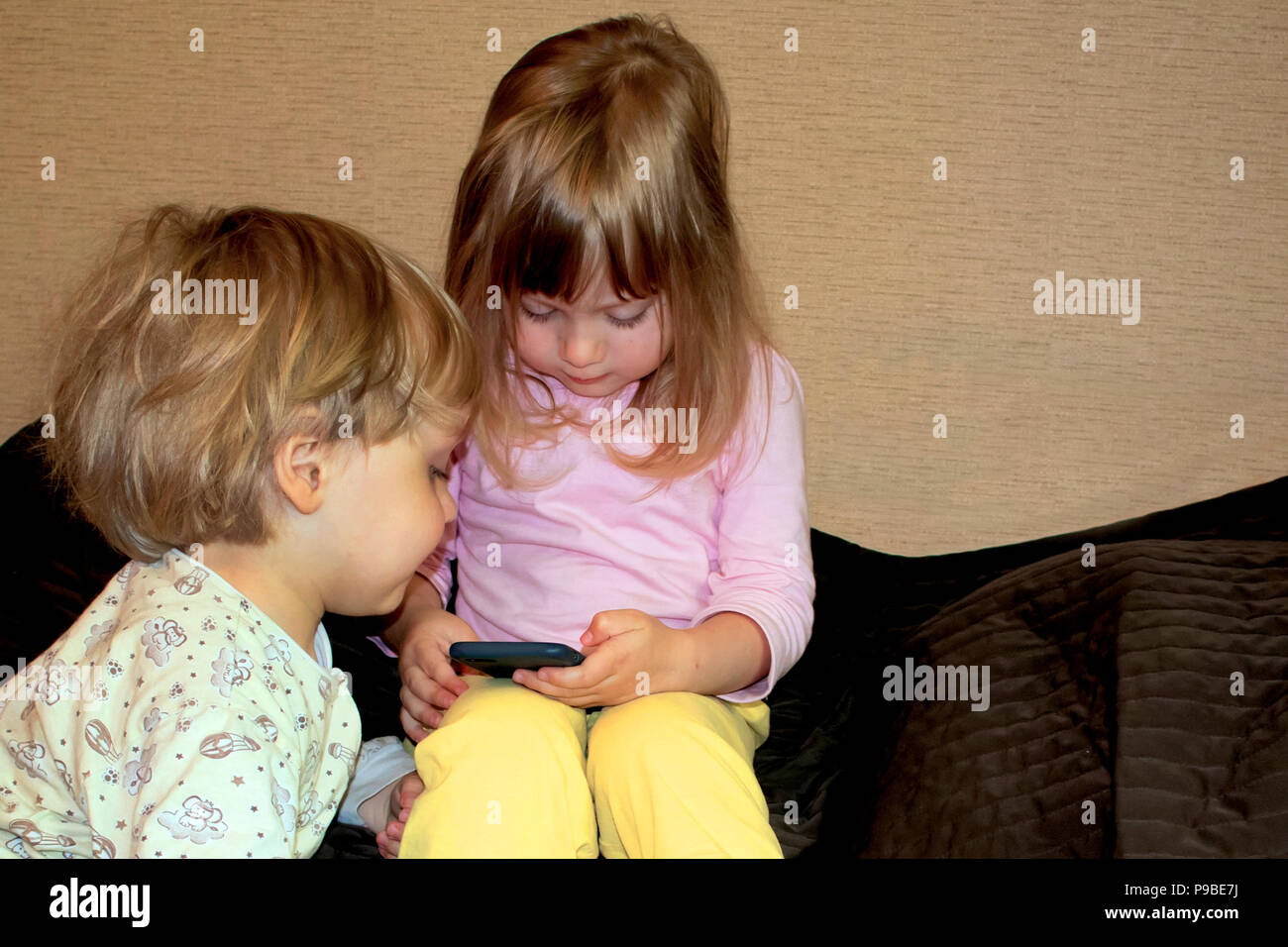 Little cute curious blonde twins watch cartoons on smartphone Stock Photo