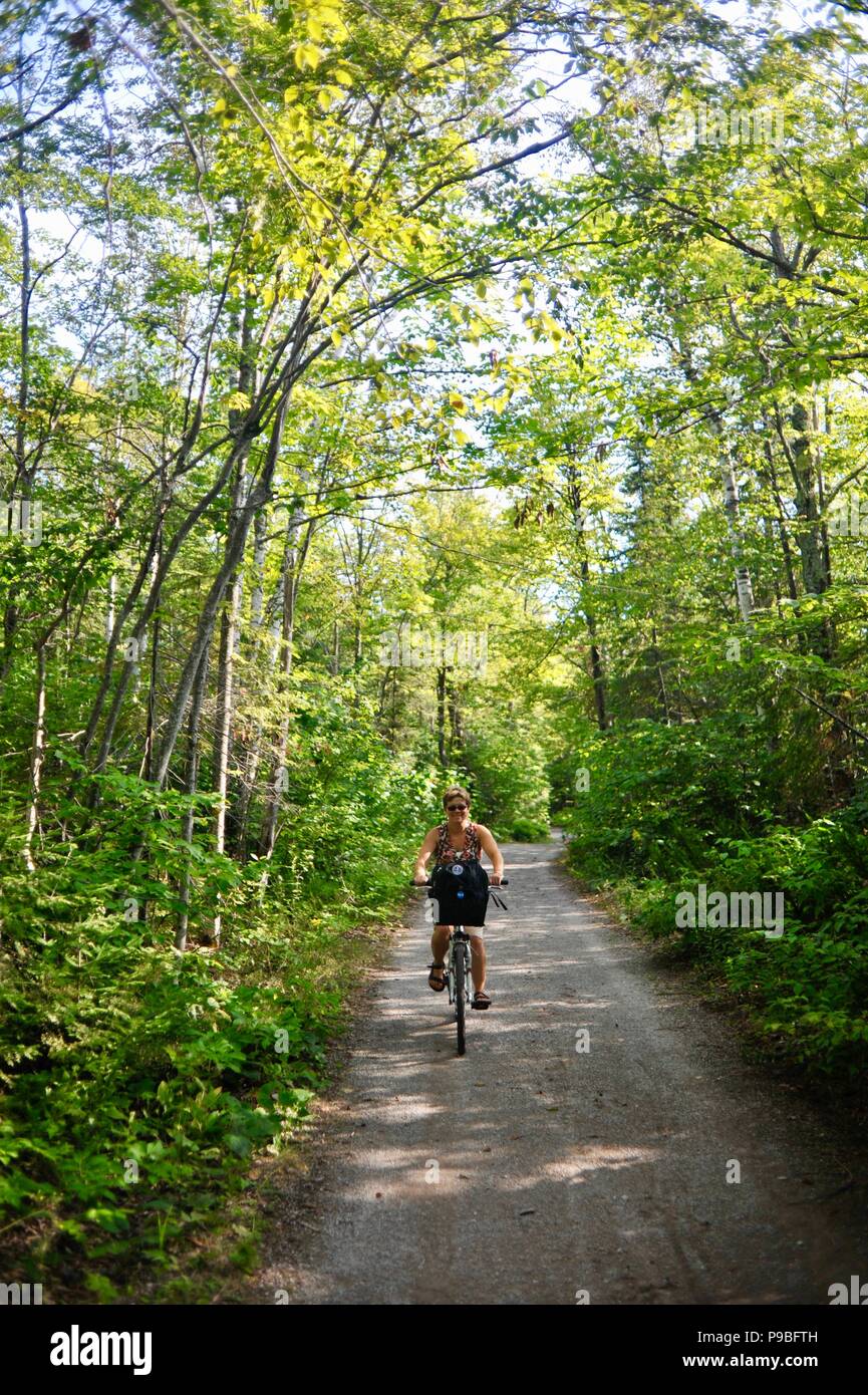 Woman bicycling on bike path that circles the entire Mackinac Island, a popular vechile-free (no cars) tourist destination in Michigan, USA. Stock Photo
