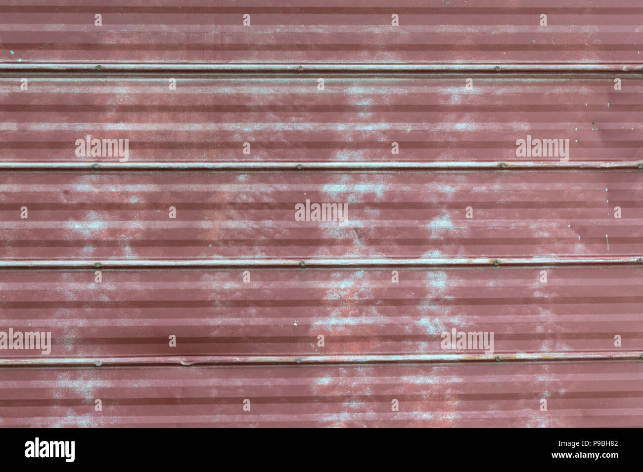 Faded peeling rusty steel sheets with oxblood red paint. Grunge