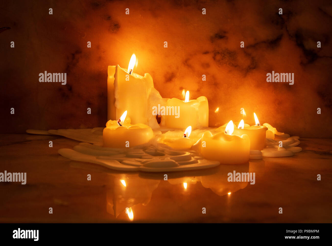 Melting wax on lighted candles reflected on a marble surface in an