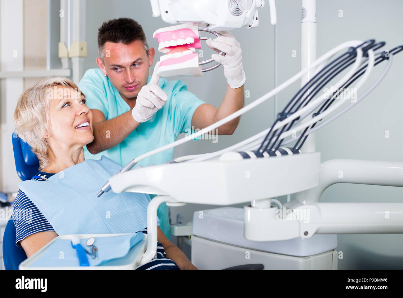 professional male dentist explaining future treatment to female patient on dental model in the