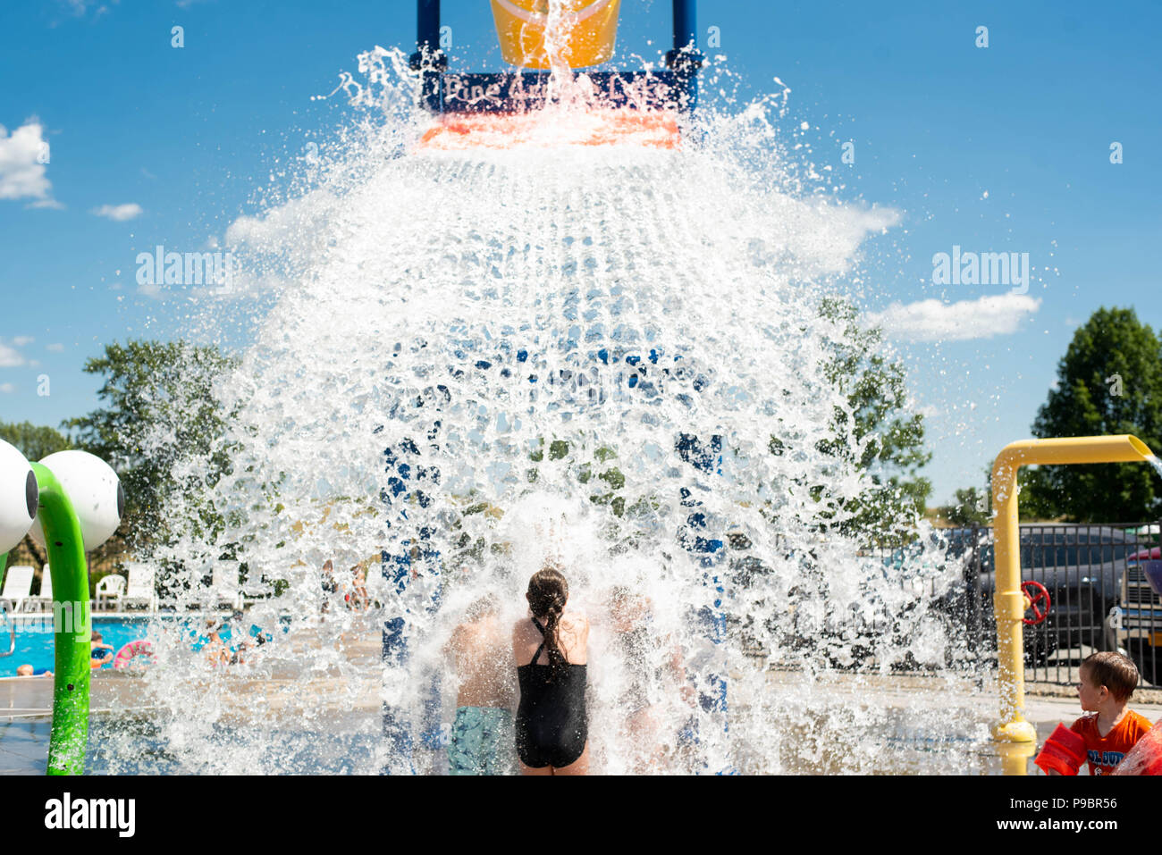 A young girl stands under falling water at a water park during the ...