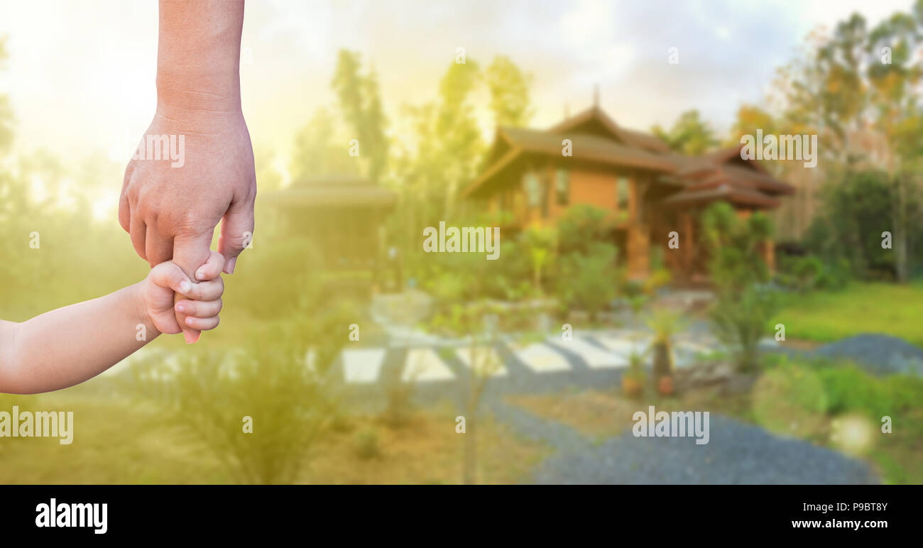 Children's hand and adult hand holding together over blur background of new wood house, dreaming
