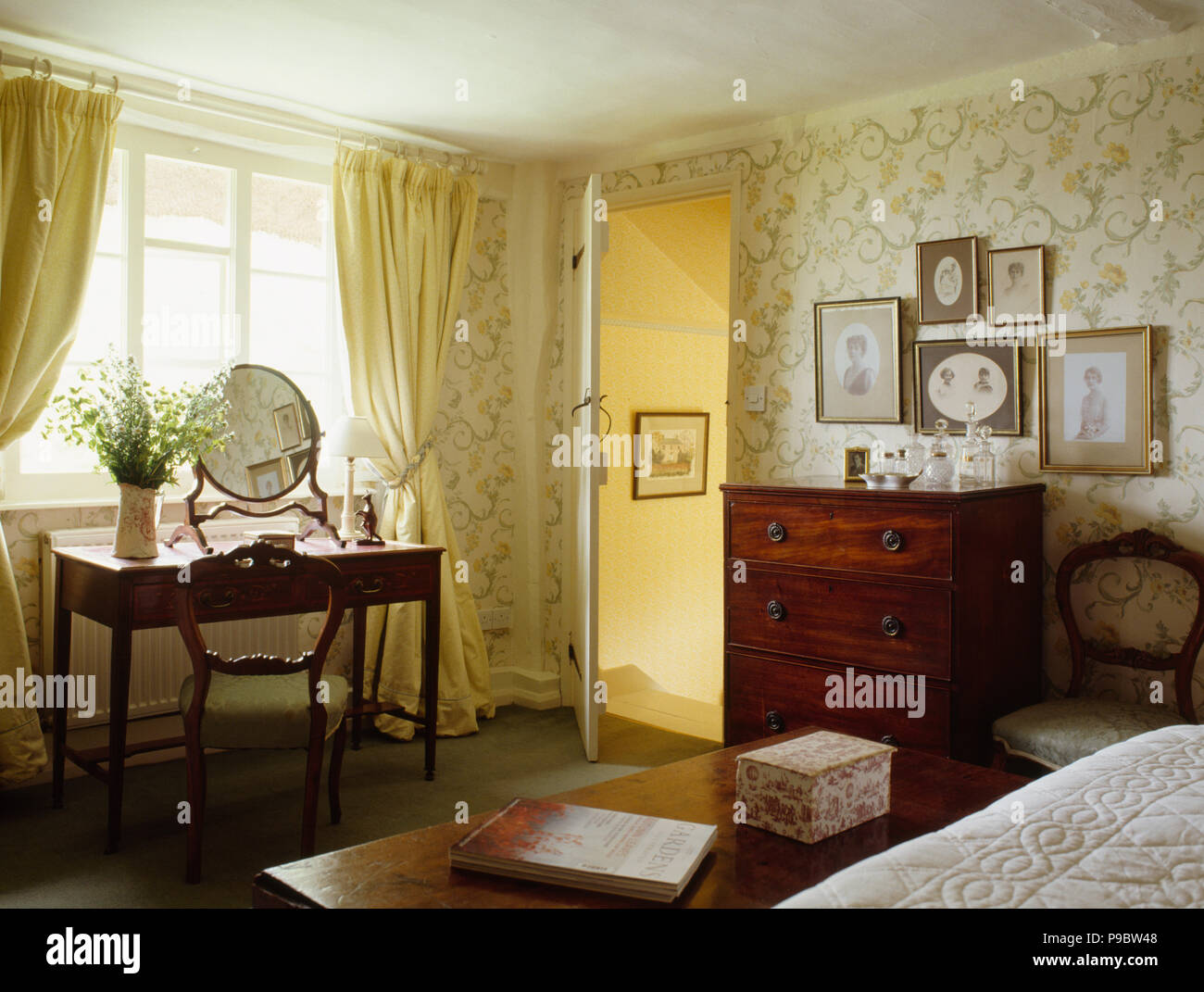 Antique chair and small table in country bedroom with pastel yellow curtains and yellow floral wallpapere Stock Photo