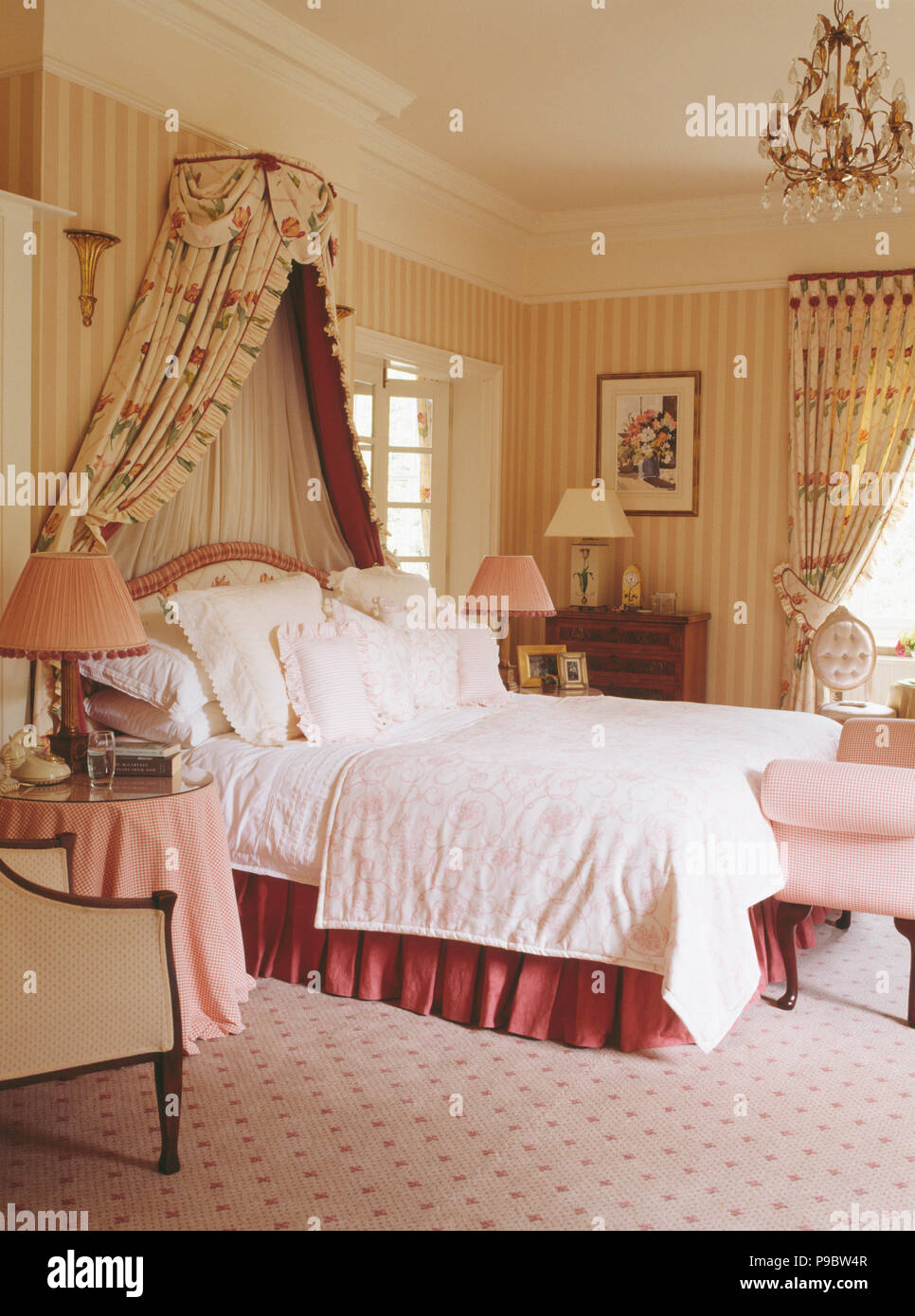 Coronet with floral drapes above bed in country bedroom with striped wallpaper Stock Photo