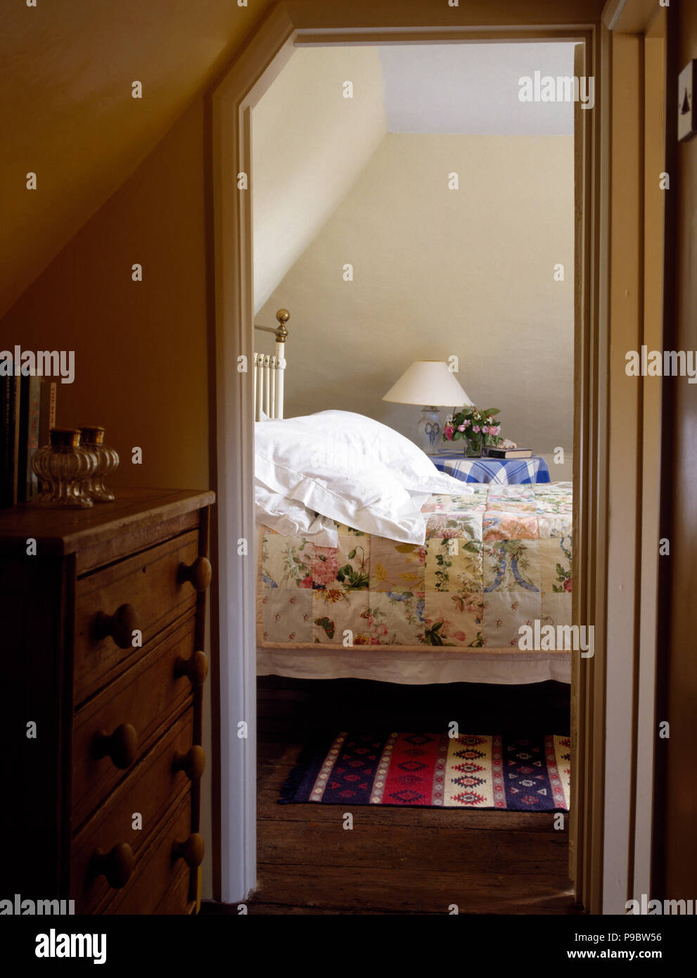 Door open to a cottage bedroom with a floral patchwork quilt on the bed Stock Photo