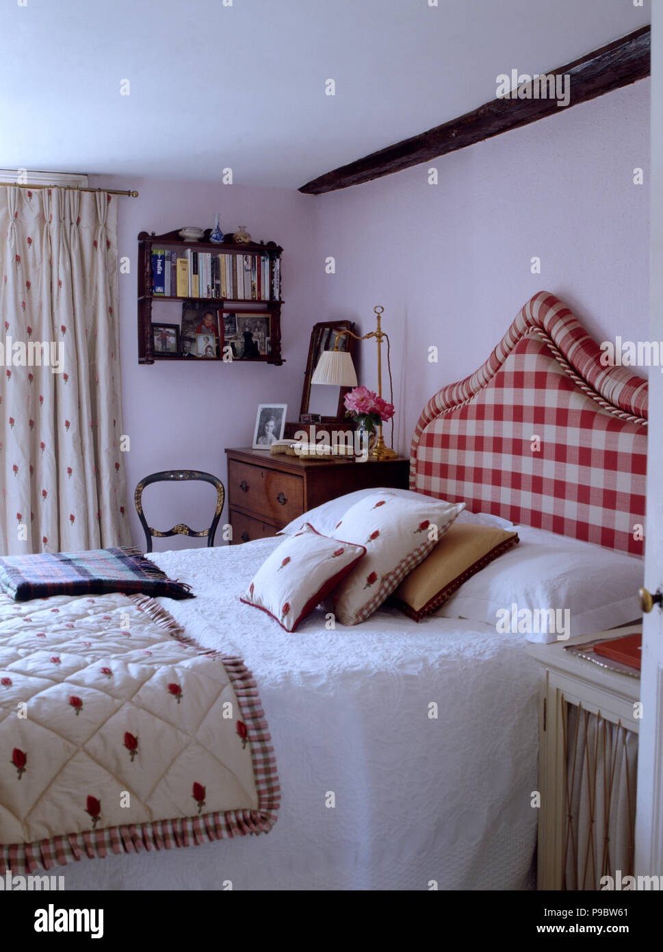 Red+white upholstered headboard on bed with patterned quilt and matching cushions in white cottage bedroom Stock Photo