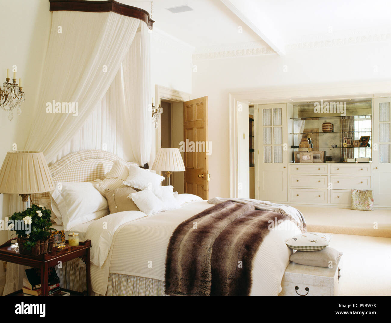 Coronet with white drapes above bed with faux fur throw Stock Photo