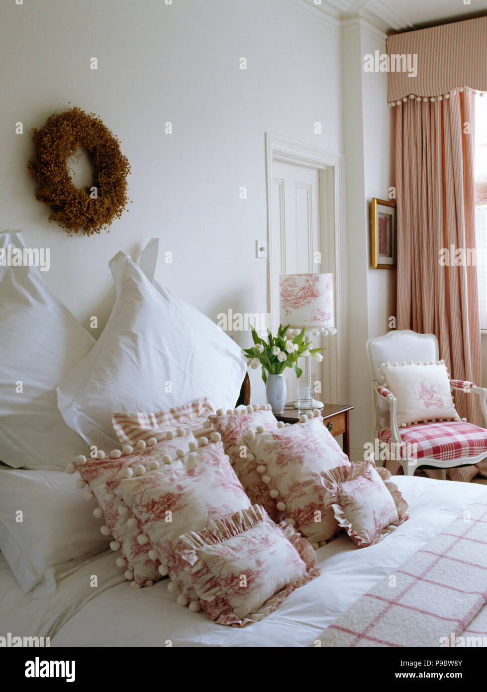 Twig wreath on wall above bed with pink Toile-de-Jouy cushions and white pillows Stock Photo