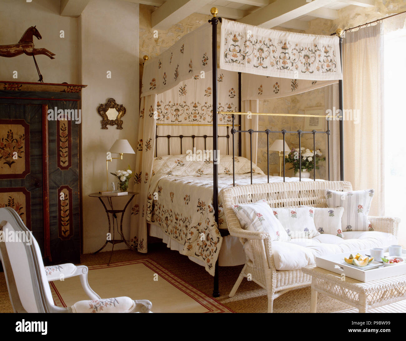 Floral patterned cream drapes with matching bed-cover on metal four-poster bed in Provencal bedroom Stock Photo