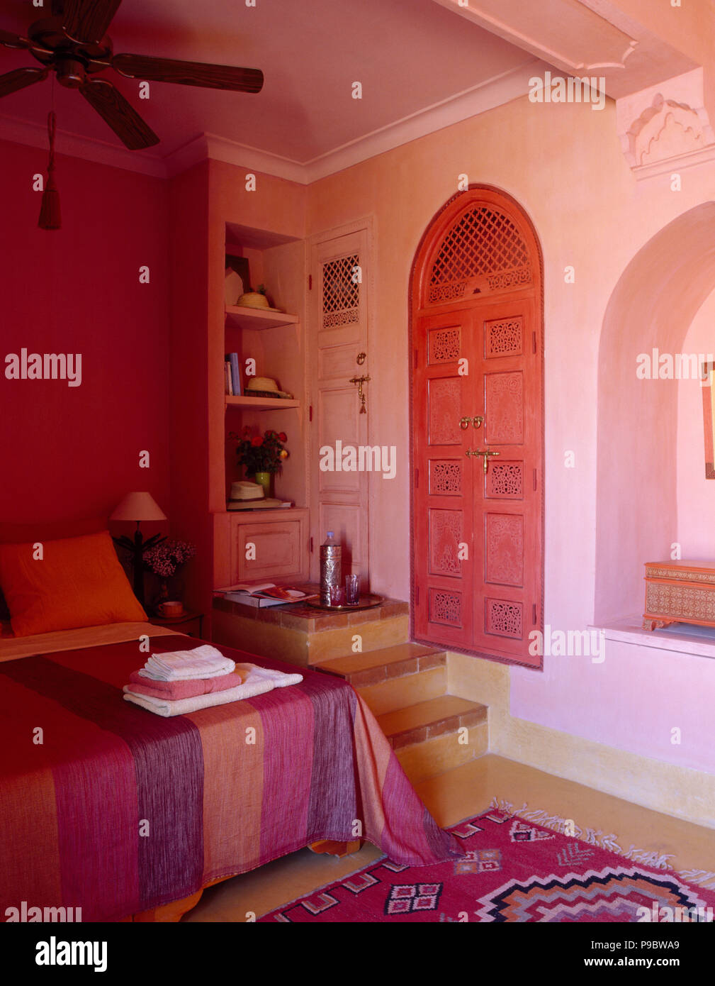Tiled steps to shelves beside bed with brightly striped cotton cover in